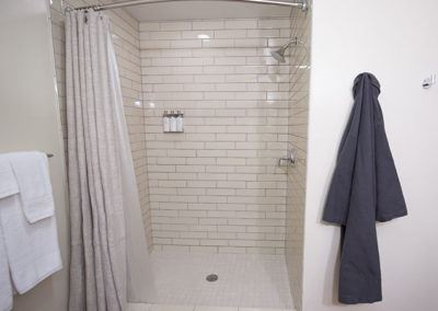 Bathroom Shower that is tiled with towel rack on one side and robe hanging on the other