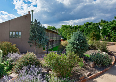 Back exterior of long hotel building porches overlooking desert landscaping and purple flowers surrounded by green trees