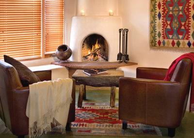 Two sofa chairs with throw blankets on them and a wooden table in front of a kiva style fireplace