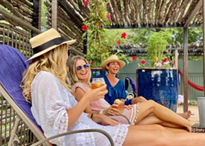 Three women sipping drinks with fruit on lounge chairs by the pool