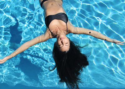 A woman wearing a black bikini floating on her back in an outdoor pool