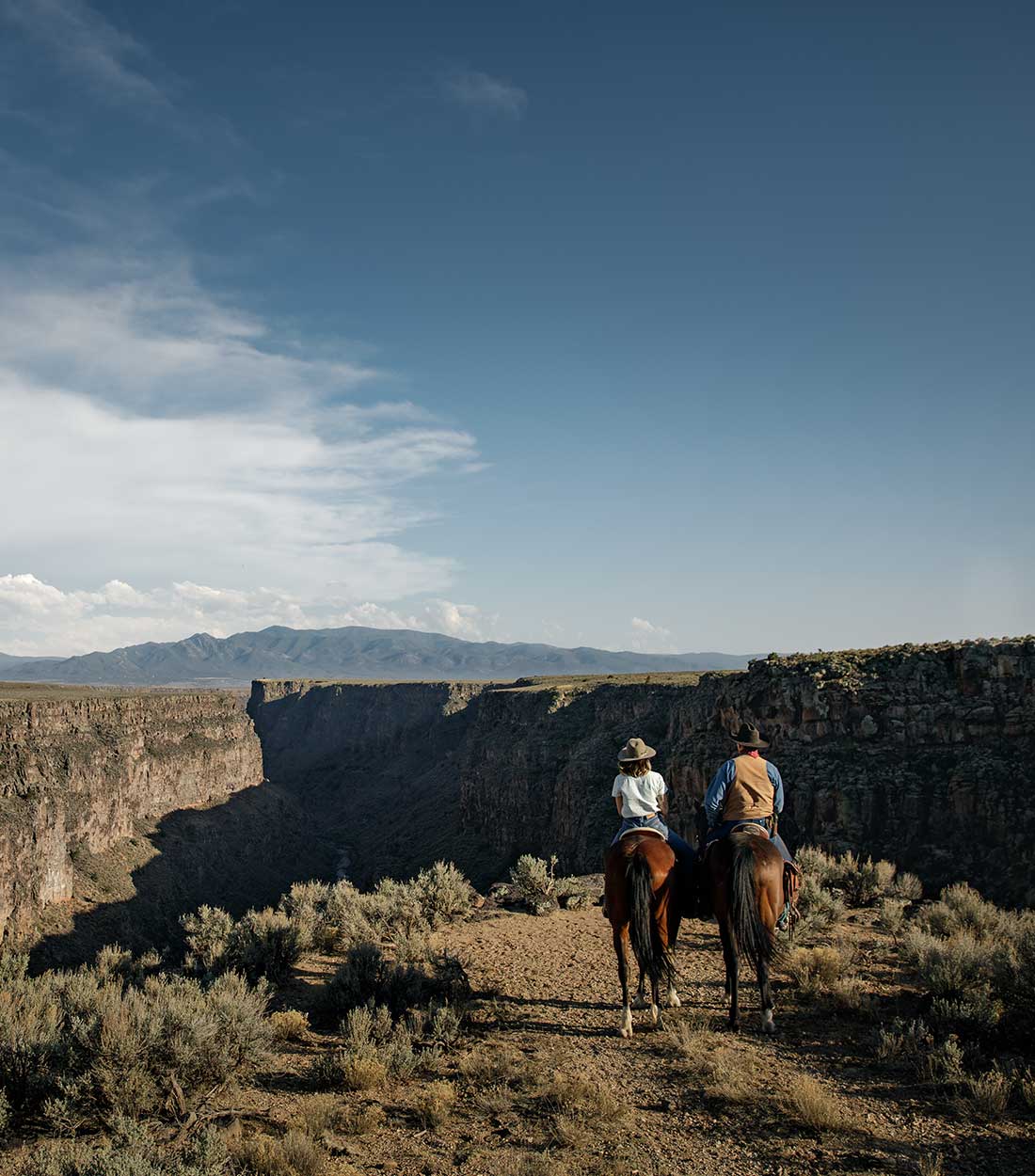 two people on two horses overlooking gorge and mountain