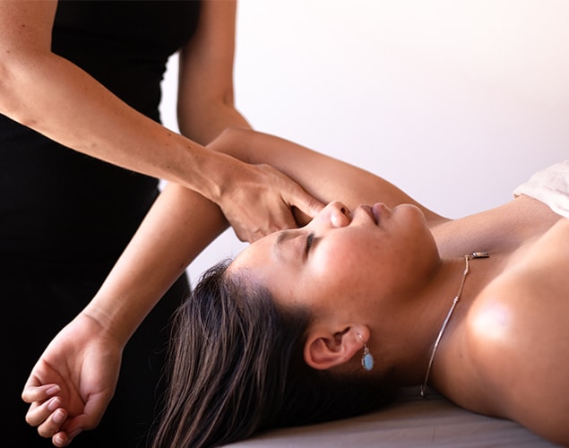 Ojo Caliente-Resort_0007_spa portrait A person is lying down with eyes closed while another person, seen partially from the torso, applies pressure to their forearm. The person receiving the treatment is wearing a necklace and earrings.