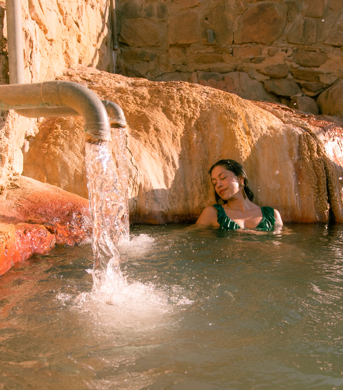 Hot Springs pools with water coming from large pottery and woman floating on her back in the center
