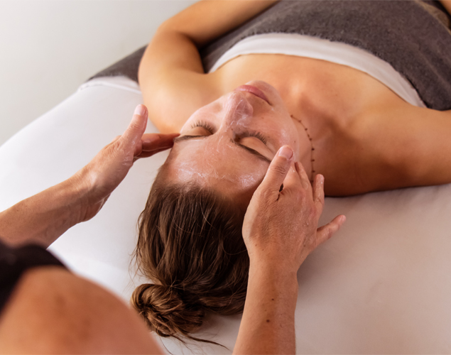 Woman lying on back on massage table with towel over her and sound therapy device on chest